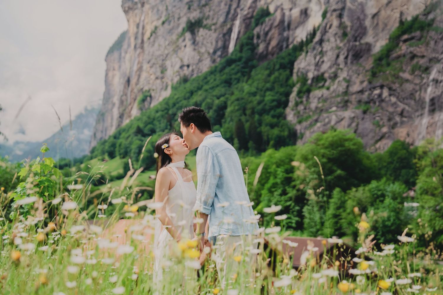 Couple shares a romantic kiss in a wildflower meadow with stunning Swiss alpine cliffs in the background.
