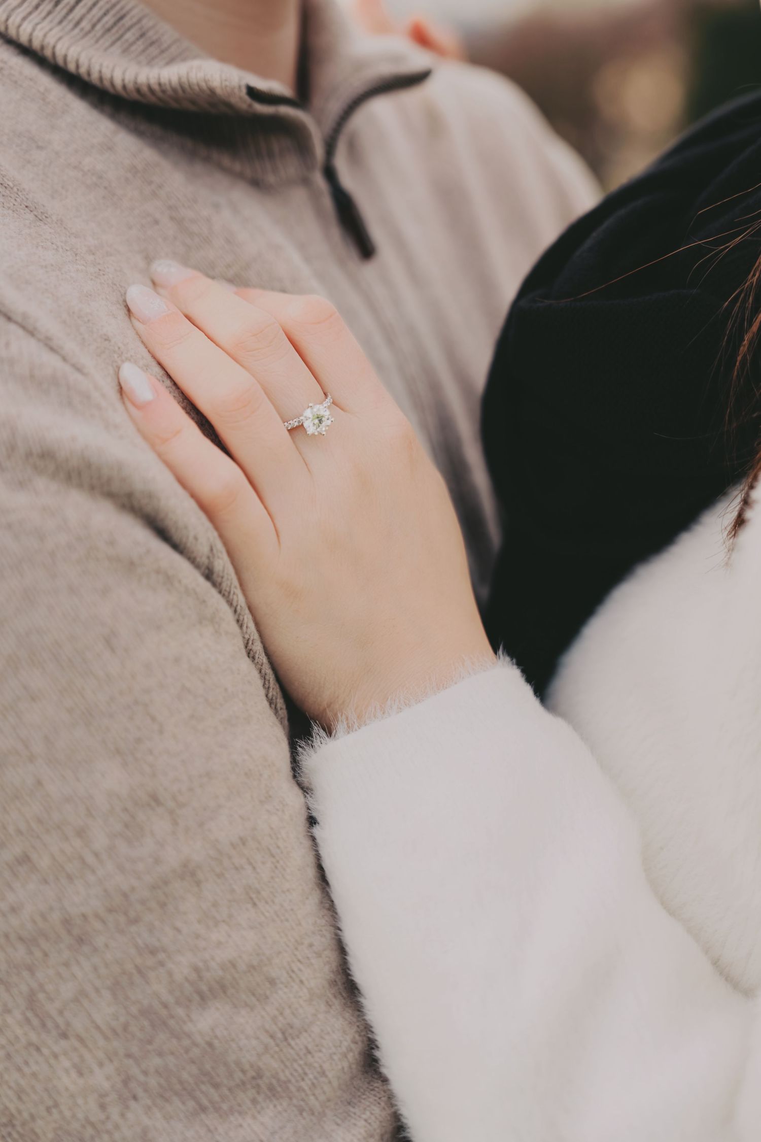 Close-up of a woman's hand displaying a stunning diamond engagement ring while embracing her partner.