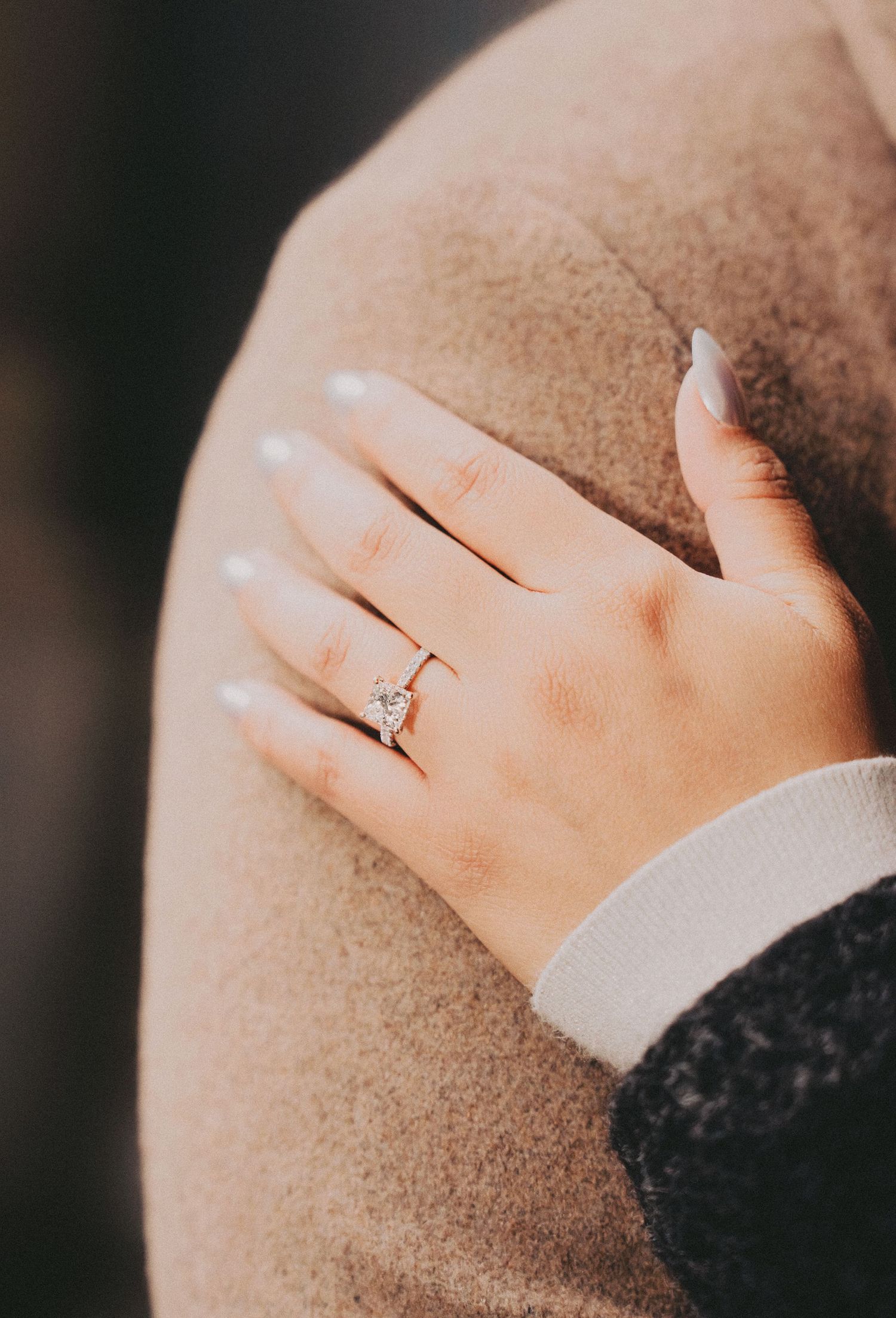 Close-up of an engagement ring with a diamond solitaire on a woman's hand with white manicured nails.