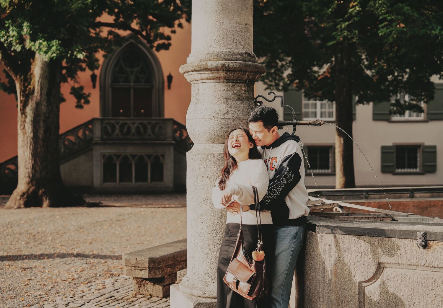 Couple sharing a romantic moment leaning against a stone fountain column in a Zurich old town square.