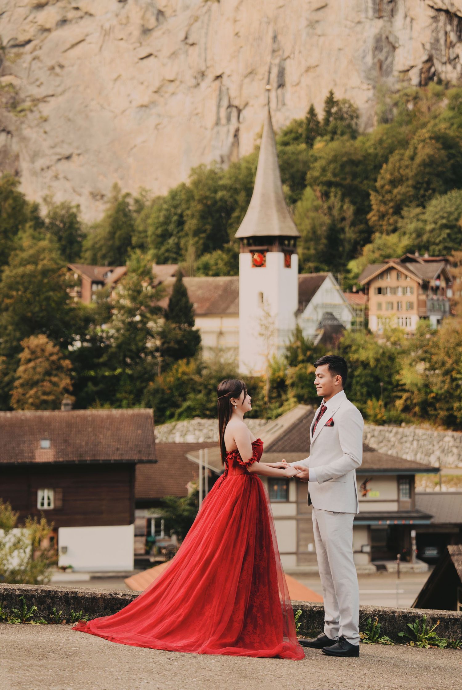 Couple exchanging vows outdoors with a white church steeple and Swiss alpine village in the background.