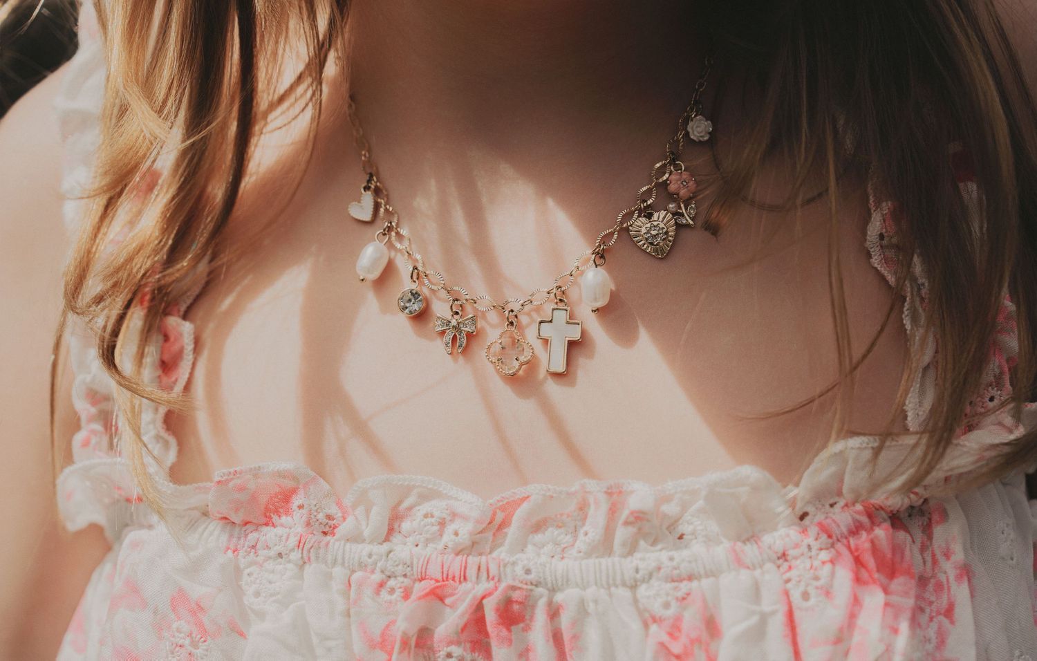 Close-up of a delicate charm necklace with cross and heart pendants on a floral dress.