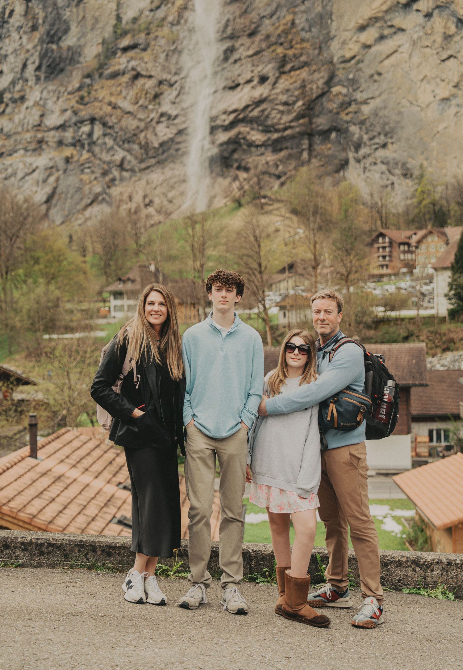 Family of four standing together with a dramatic Swiss waterfall and village behind them.