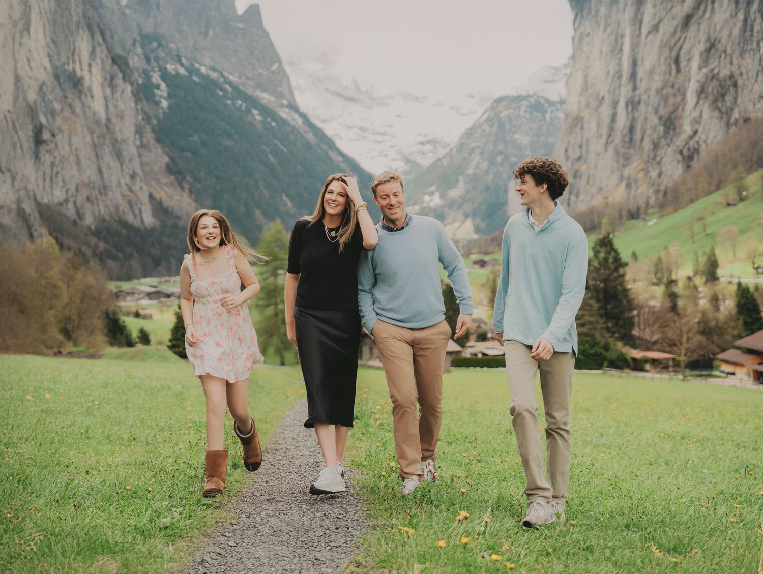 Family of four walking and laughing on a path in Lauterbrunnen valley with dramatic Swiss Alps backdrop.