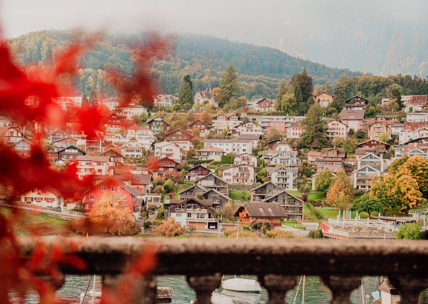 Autumn view of a Swiss village with colorful houses nestled on a hillside, framed by red fall foliage.