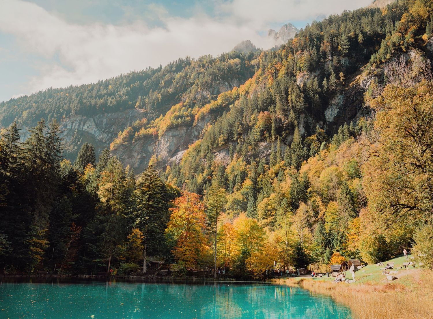 Serene turquoise alpine lake surrounded by vibrant autumn colored forest and mountain backdrop.