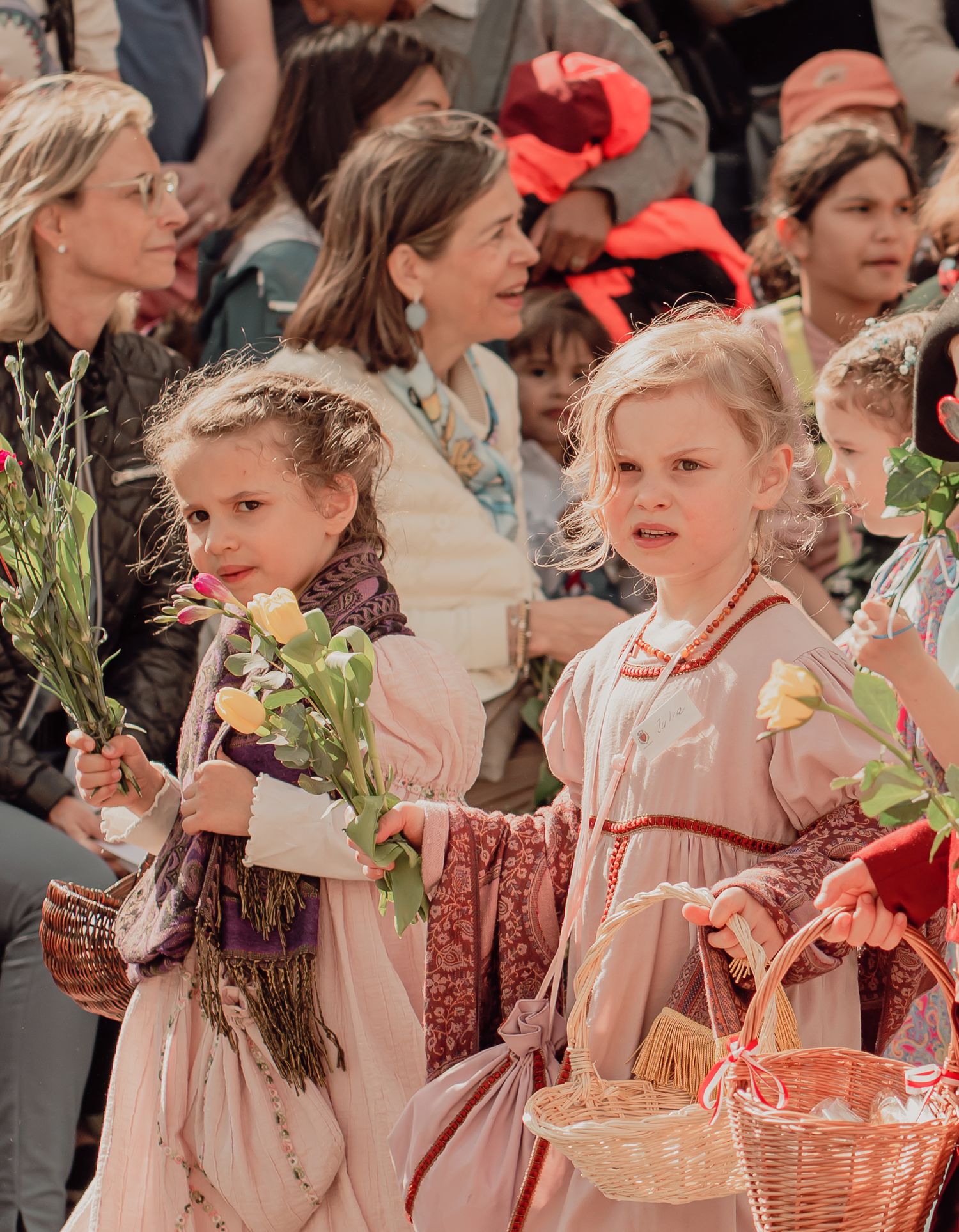 Two young girls in pink historical costumes holding flowers and baskets at a traditional festival parade.
