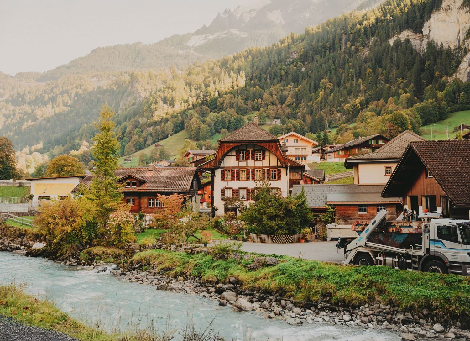 Charming Swiss alpine village with traditional wooden chalets beside a turquoise mountain river.