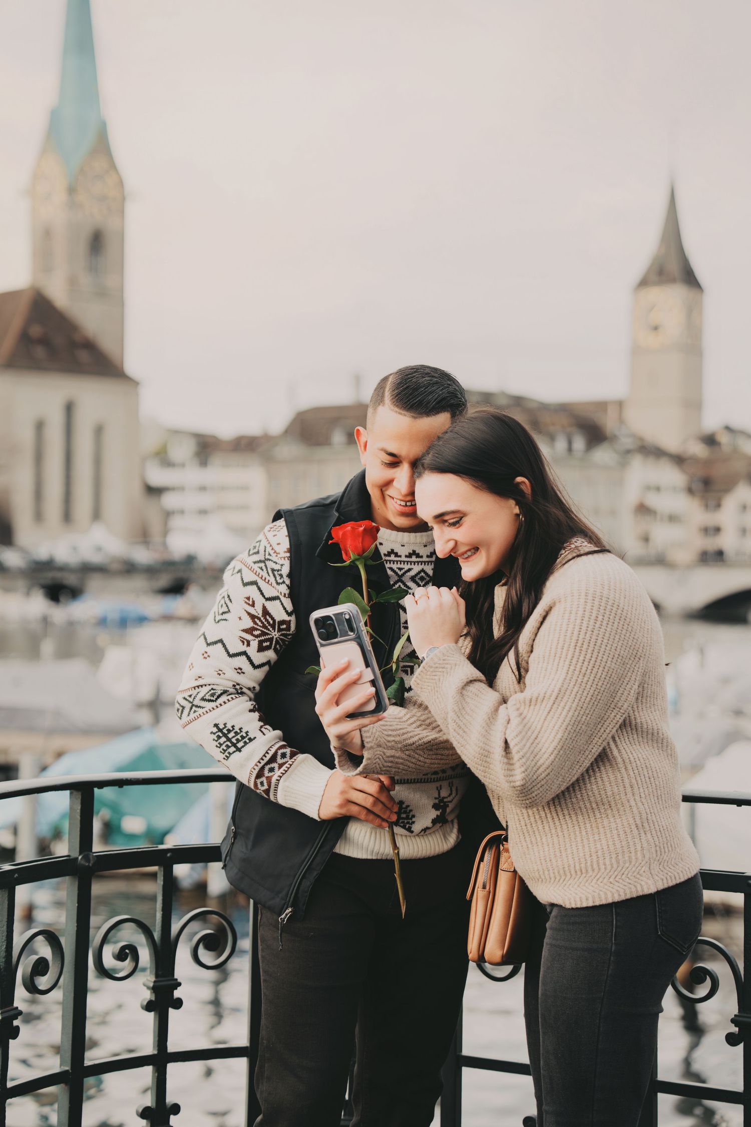 Romantic couple sharing a moment looking at smartphone holding a red rose in Zurich.