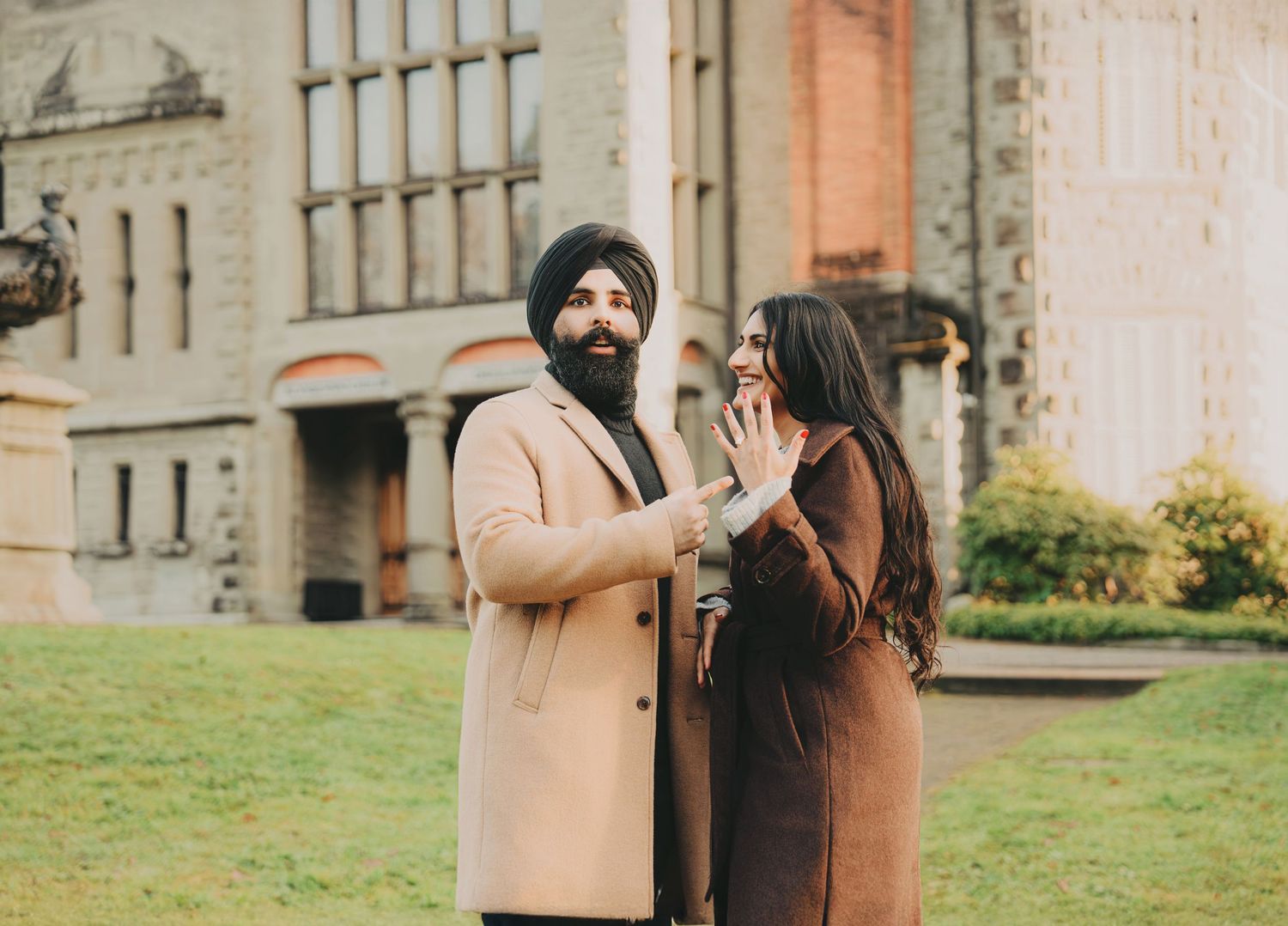 Couple sharing a joyful engagement moment on grass in front of a historic castle building.