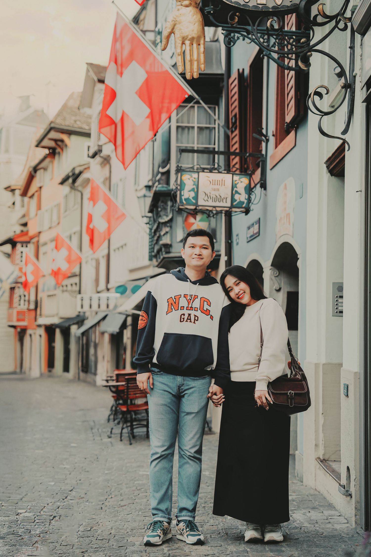 Couple posing together on a charming Zurich old town street decorated with Swiss national flags.