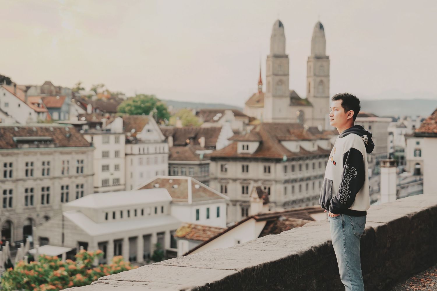 Asian man gazing at Zurich old town skyline with Grossmünster cathedral twin towers in background.