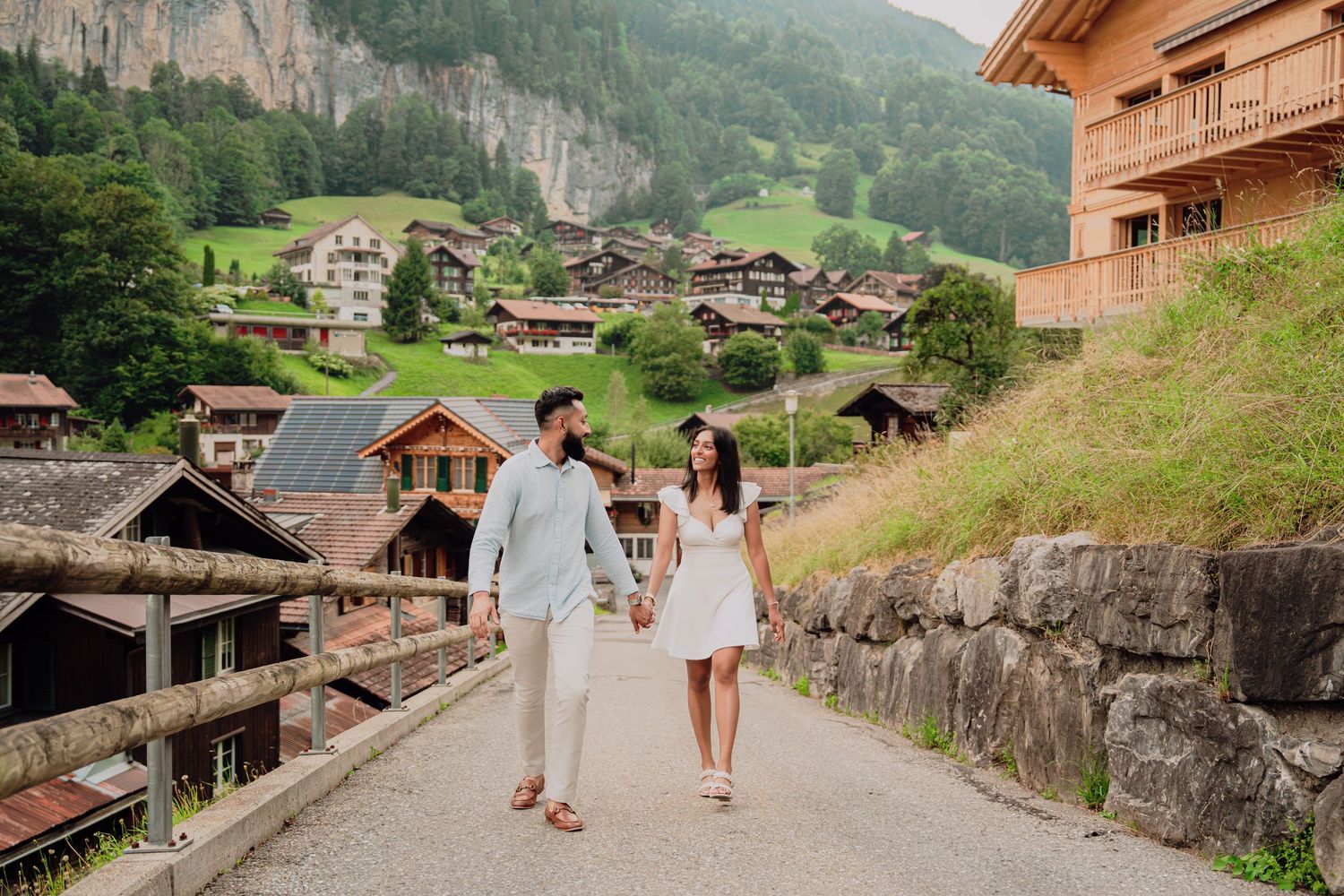 Couple walking hand in hand on a road through a picturesque Swiss village with traditional Alpine chalets.