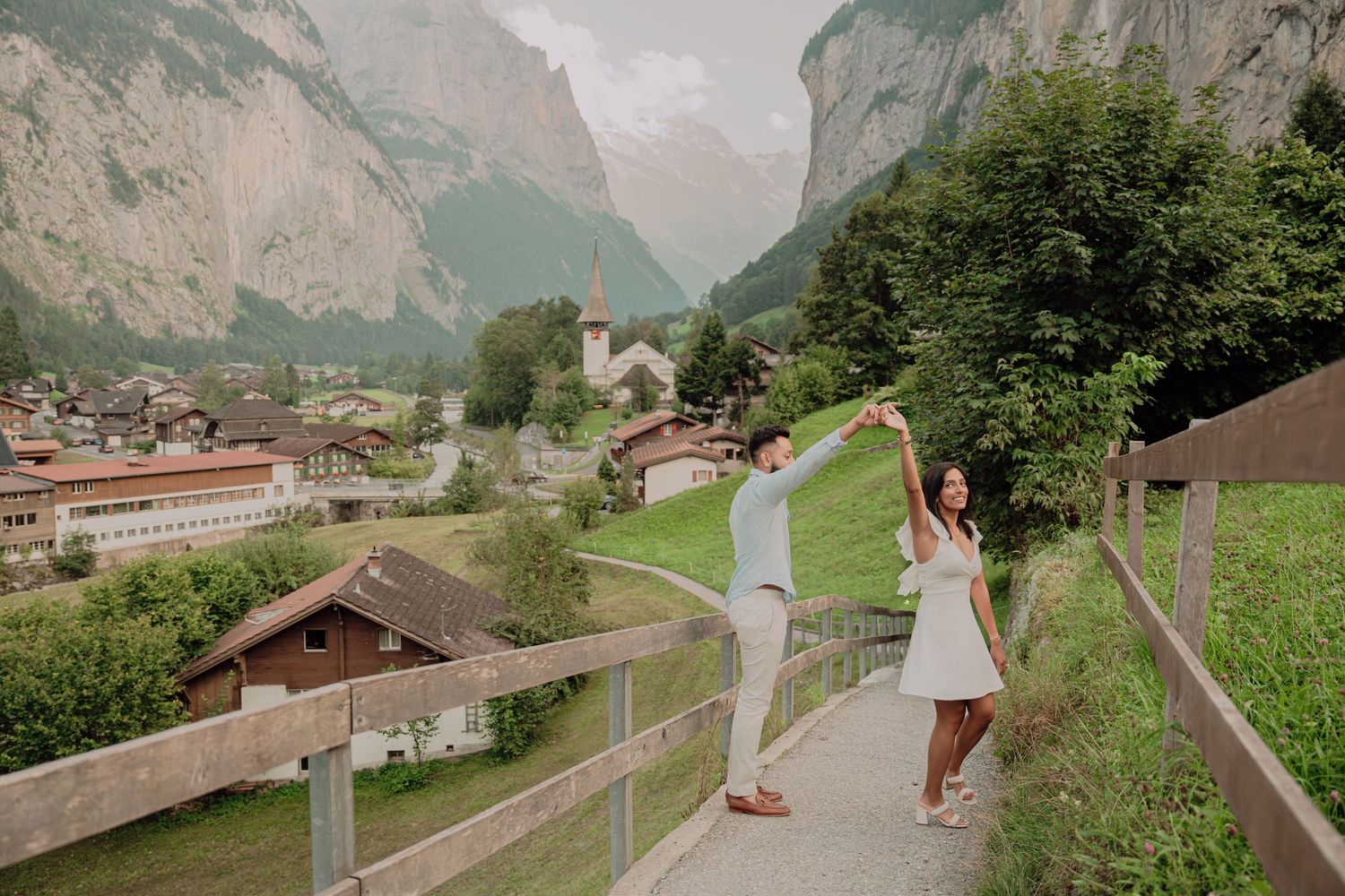 Couple dancing and spinning on a scenic overlook in Lauterbrunnen, Switzerland, with alpine village backdrop.