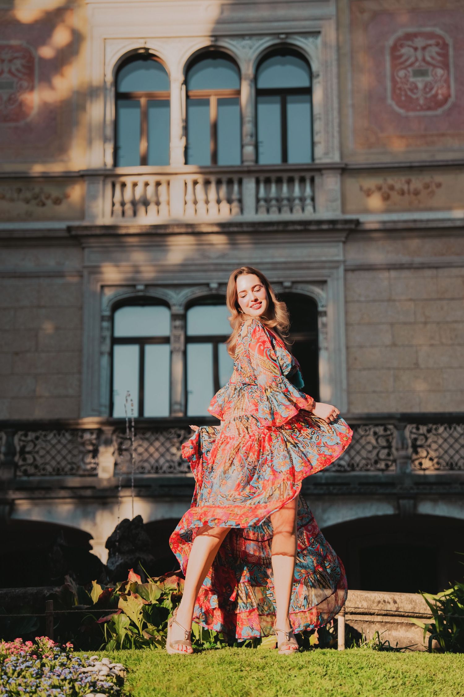 Woman in colorful floral dress twirling in front of ornate historic European building facade.