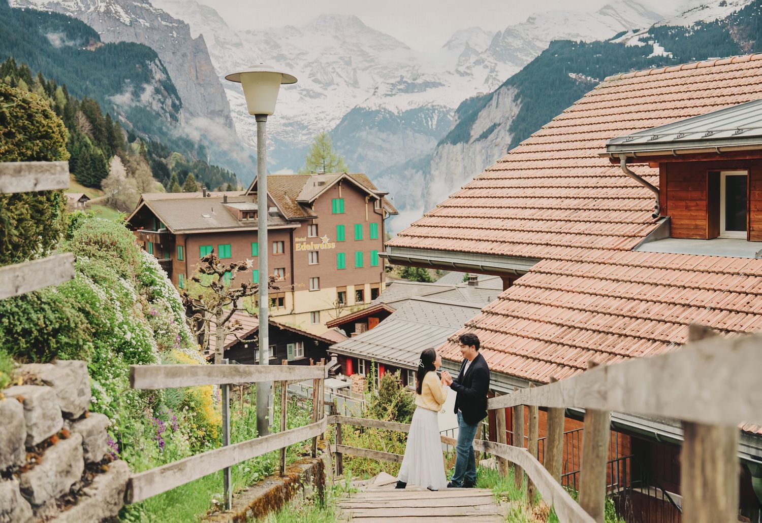 Couple sharing a tender moment on wooden stairs in a charming Swiss mountain village.