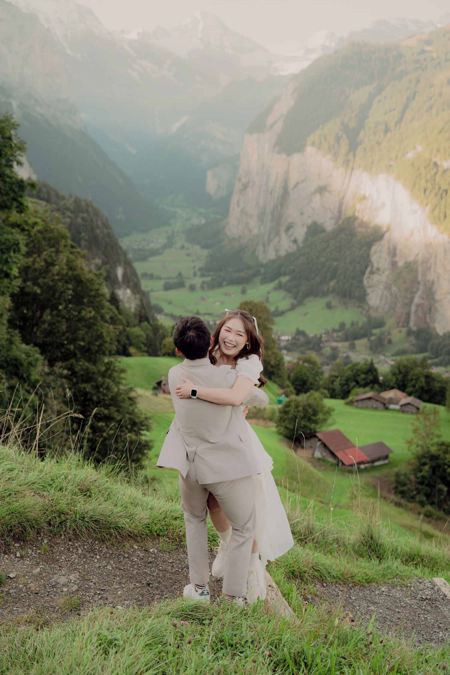 Joyful couple embracing and spinning on hillside with breathtaking Lauterbrunnen valley in background.