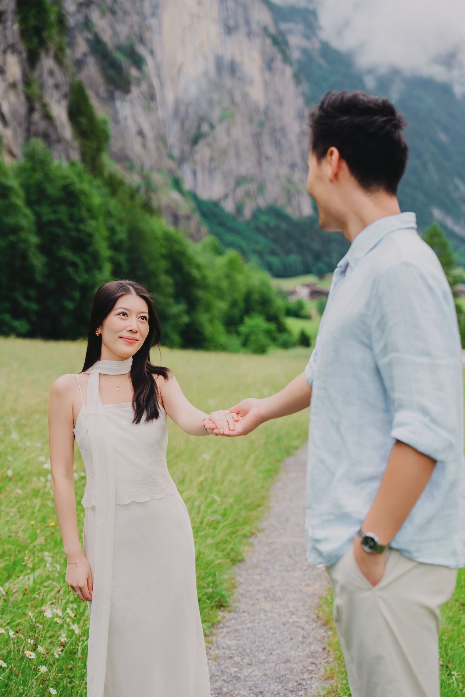 Young couple holding hands on a scenic path in a lush green Alpine valley in Lauterbrunnen, Switzerland.