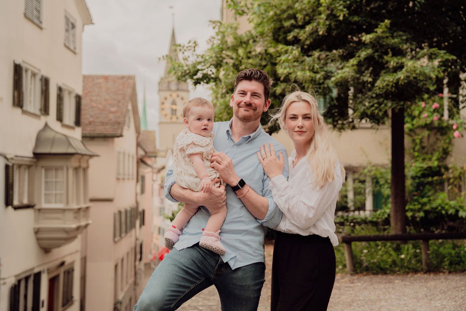 Young family with baby posing in front of historic Zurich old town buildings.