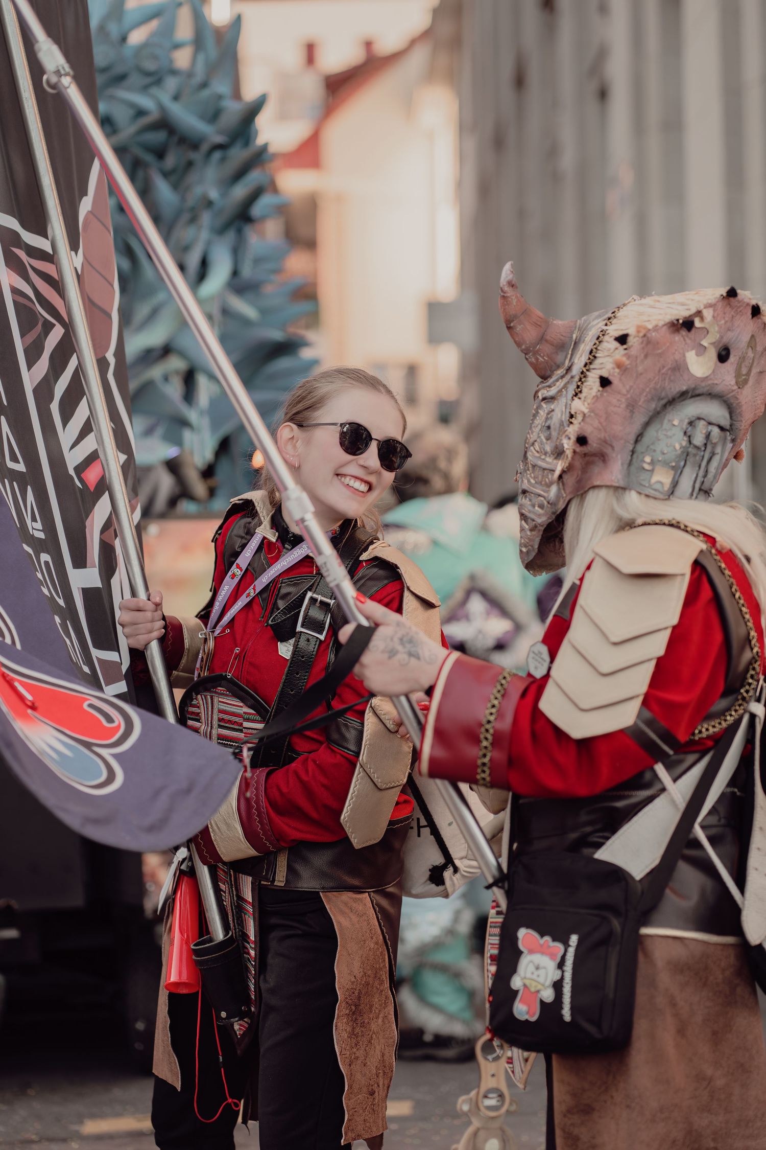 Two cosplayers in red armor costumes at a convention, one wearing sunglasses holding a banner.