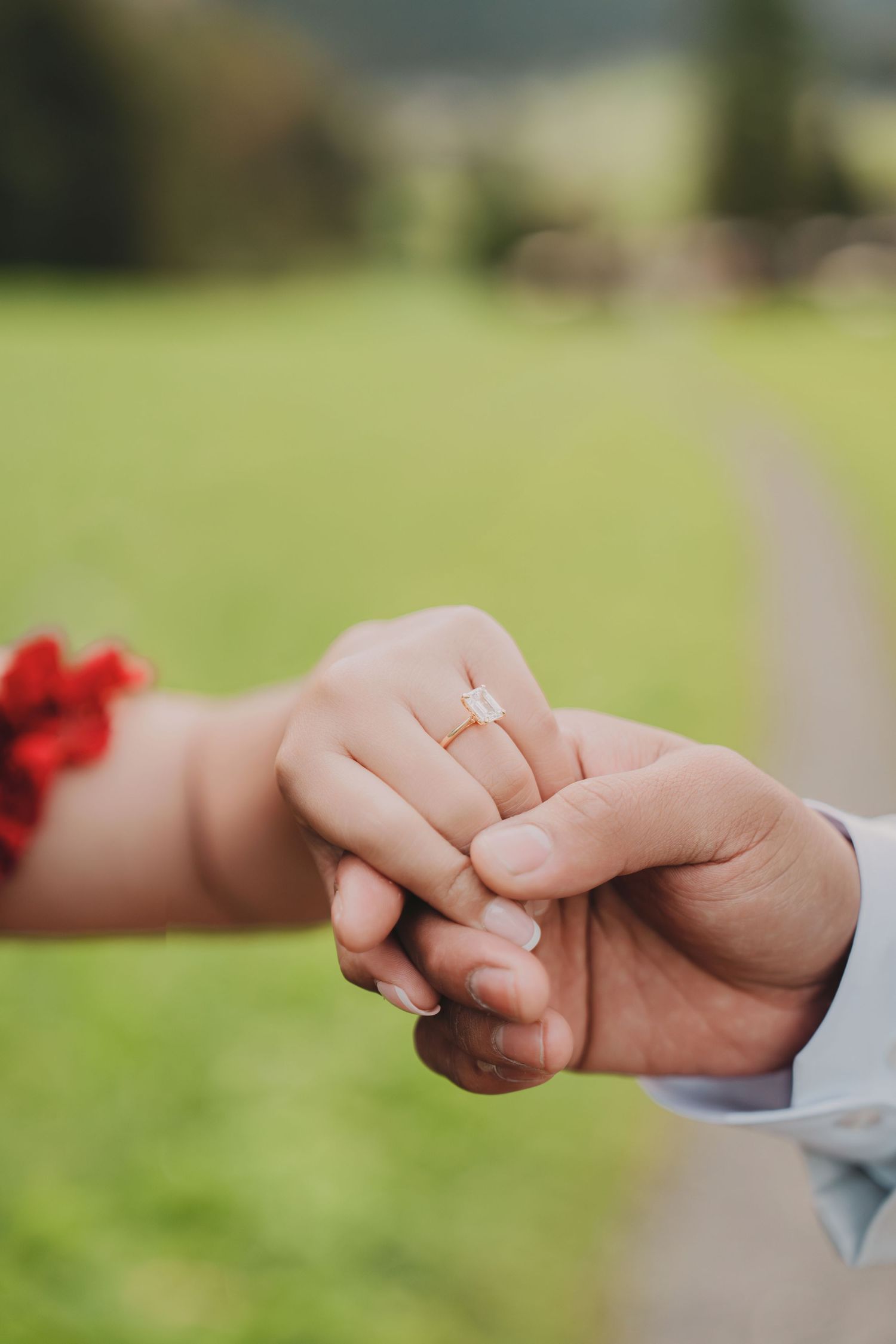 Close-up of bride's hand showing elegant diamond engagement ring held by groom outdoors.