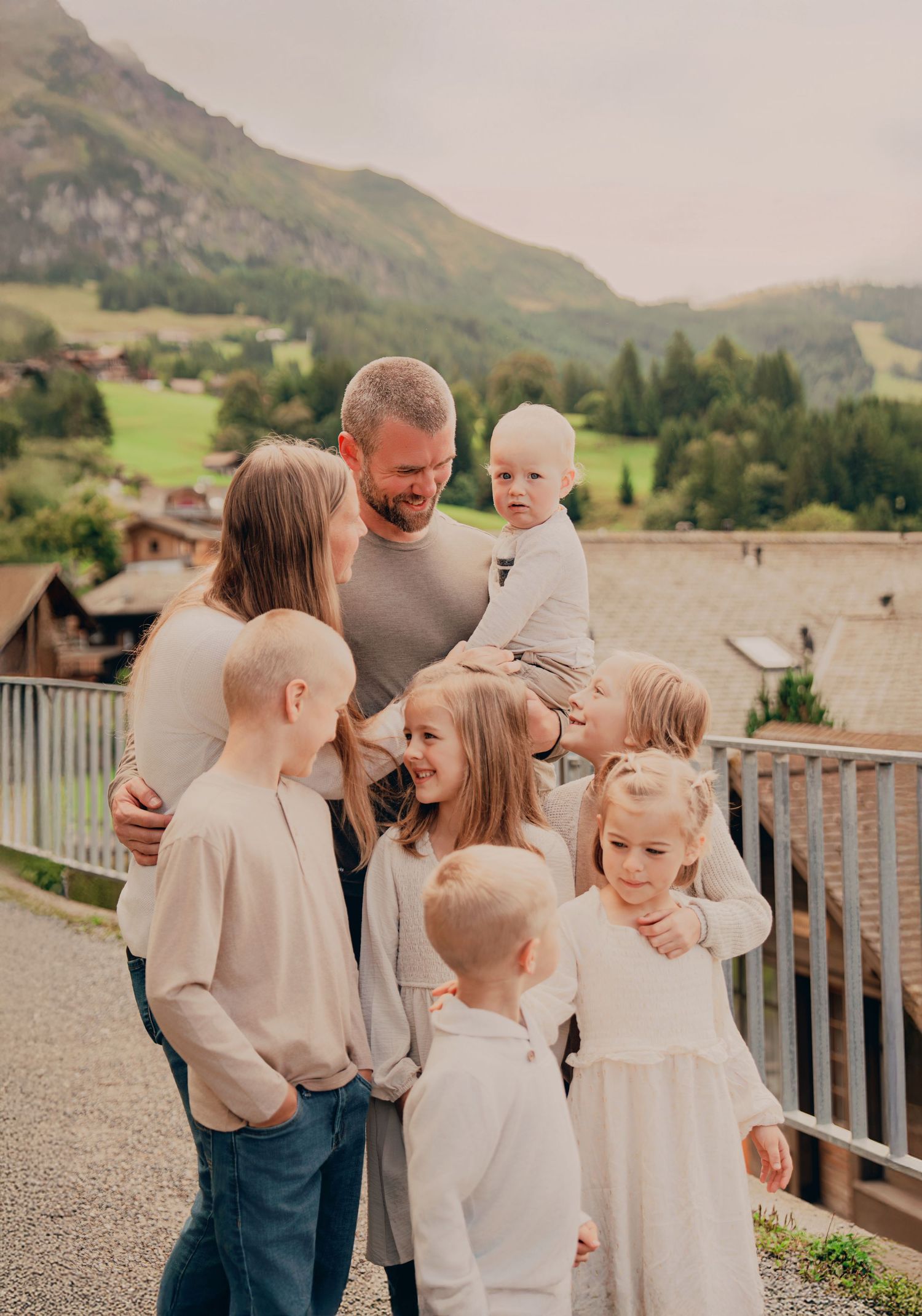 A large family with six children poses together on a mountain village path in the Swiss Alps.