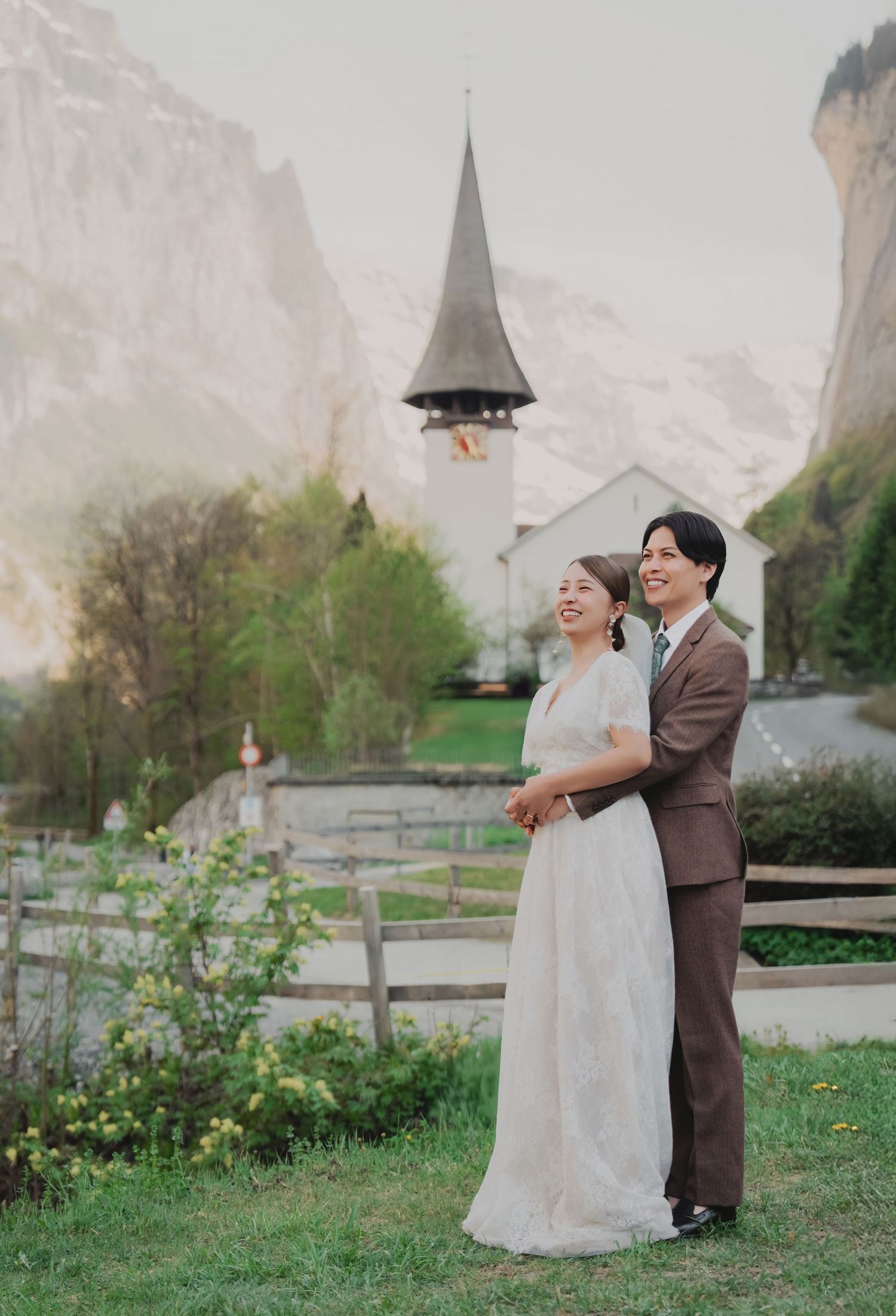 Happy couple embracing in front of a white Swiss church with dramatic mountain cliffs in Lauterbrunnen.