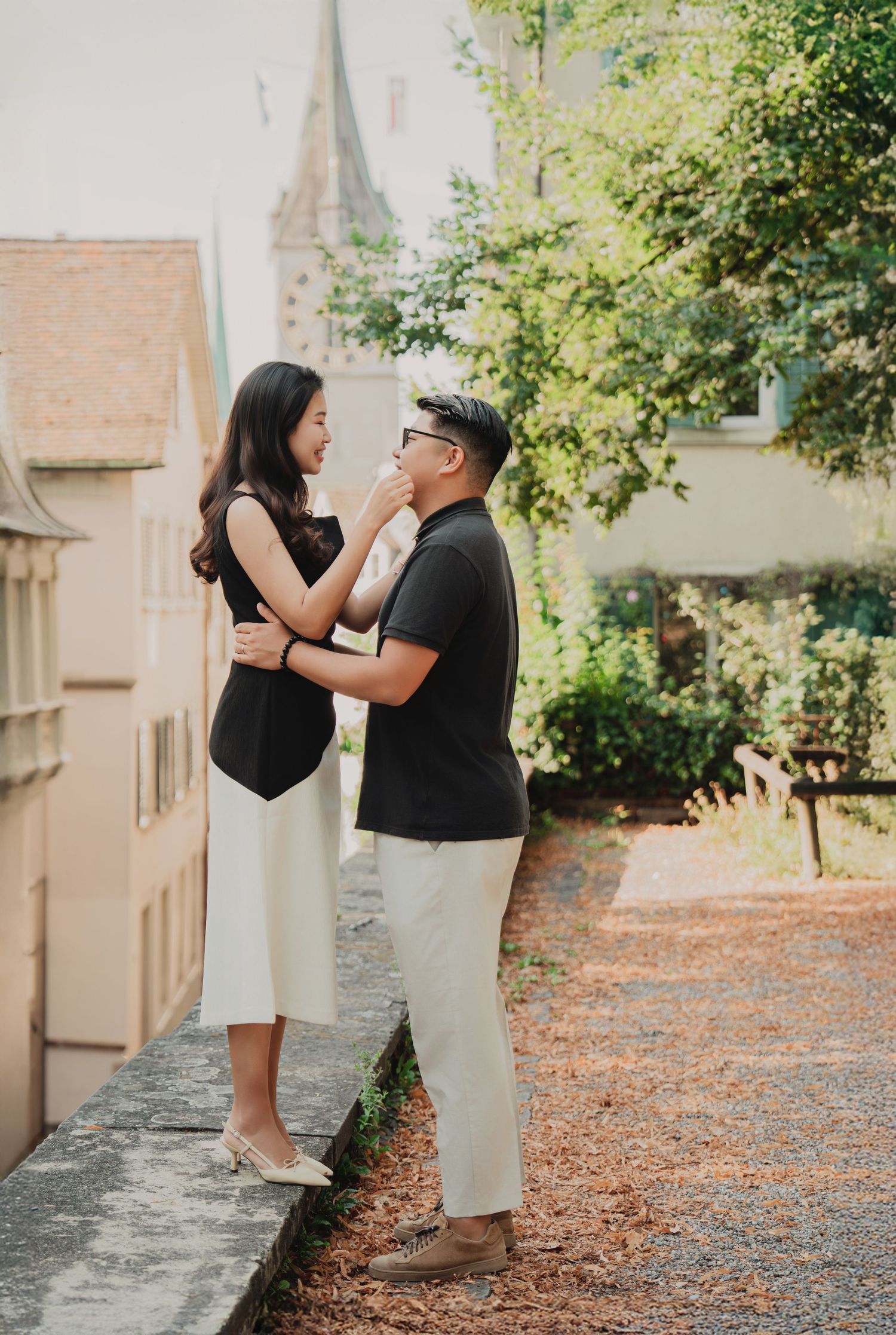 Couple sharing a tender moment in a sunlit garden near a historic church building in Zurich.