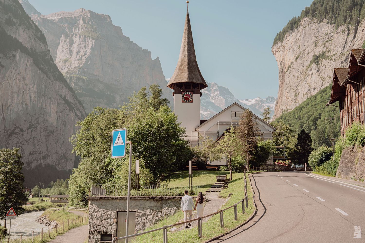 Charming Swiss village street with a historic church steeple framed by dramatic alpine cliffs.