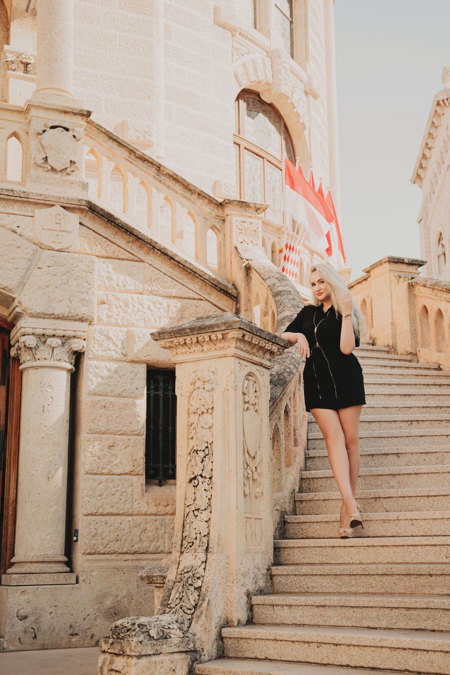 Blonde woman descending ornate stone staircase of historic Monaco courthouse building.