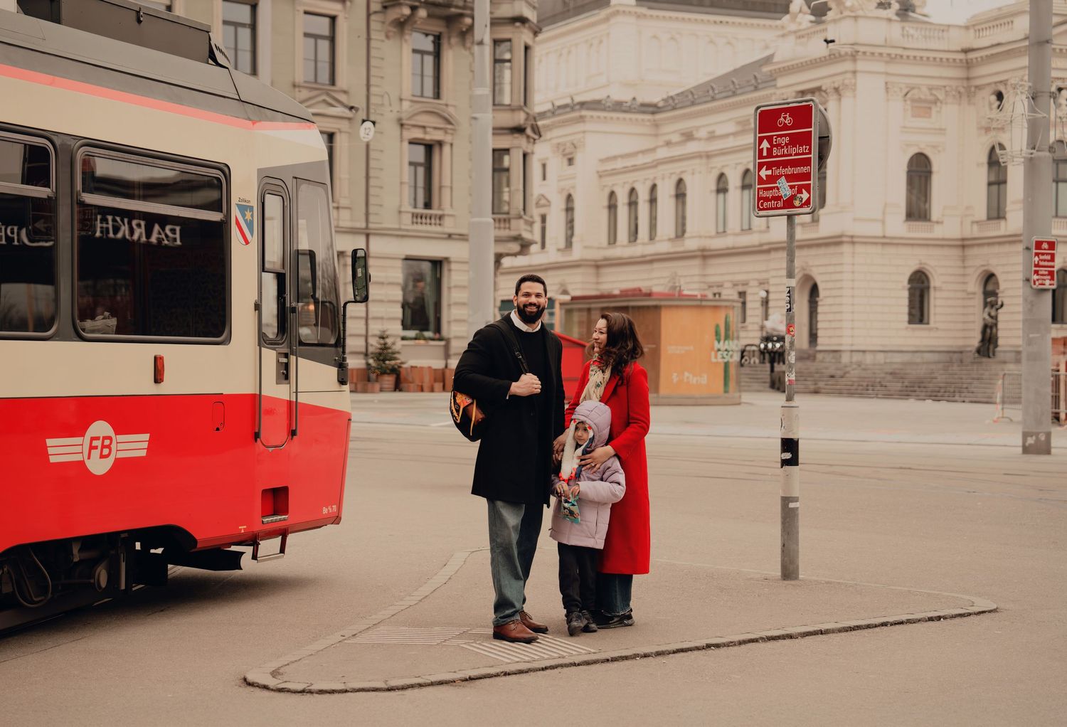Couple with child posing near a red tram on a European city square in winter.
