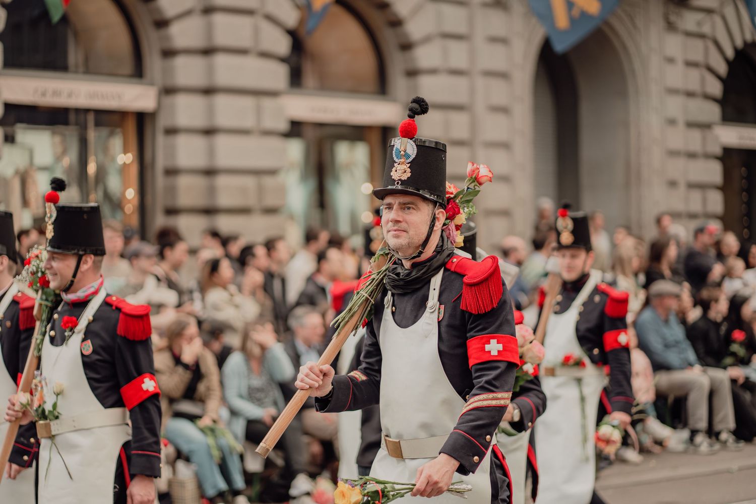 A man in historic black and white military uniform carries roses in a traditional street parade.