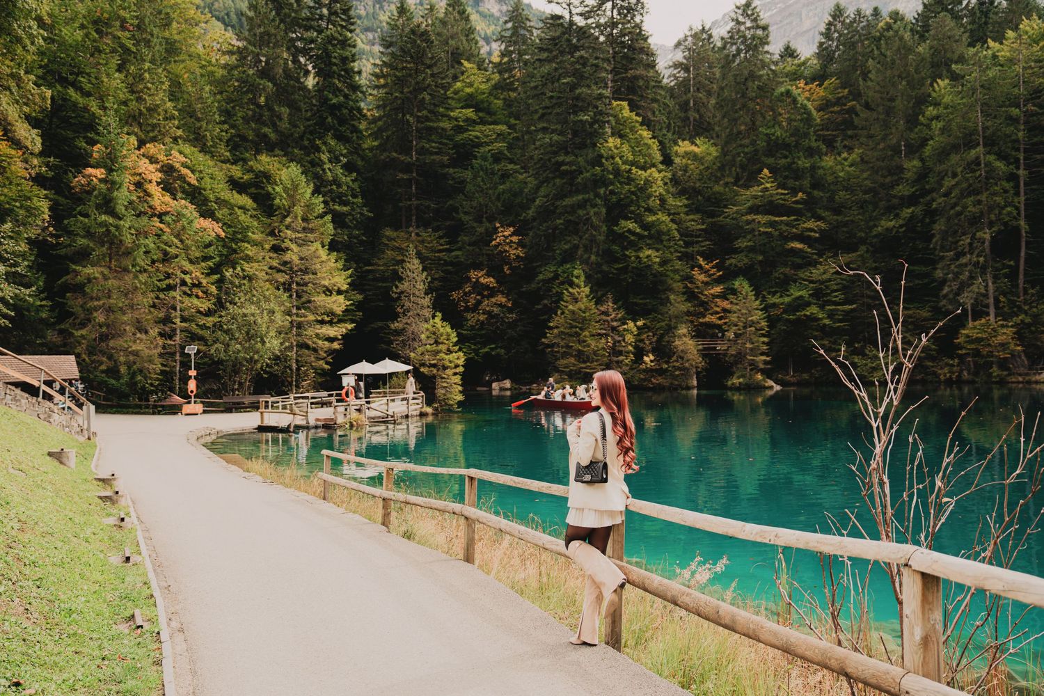 Woman with red hair standing by turquoise mountain lake surrounded by autumn forest trees.