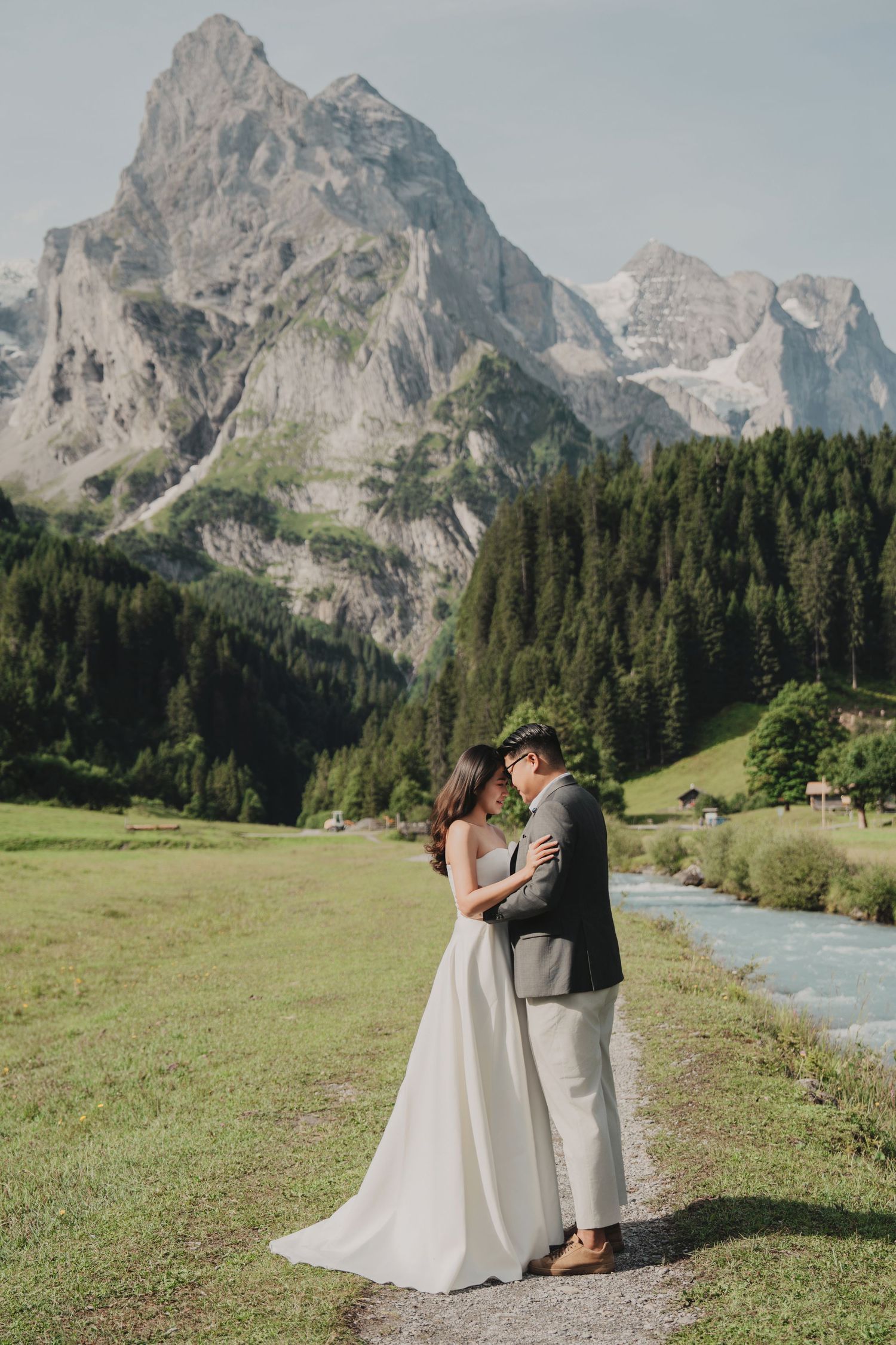 Bride and groom sharing a tender embrace on a scenic alpine path with a glacier-capped mountain backdrop.