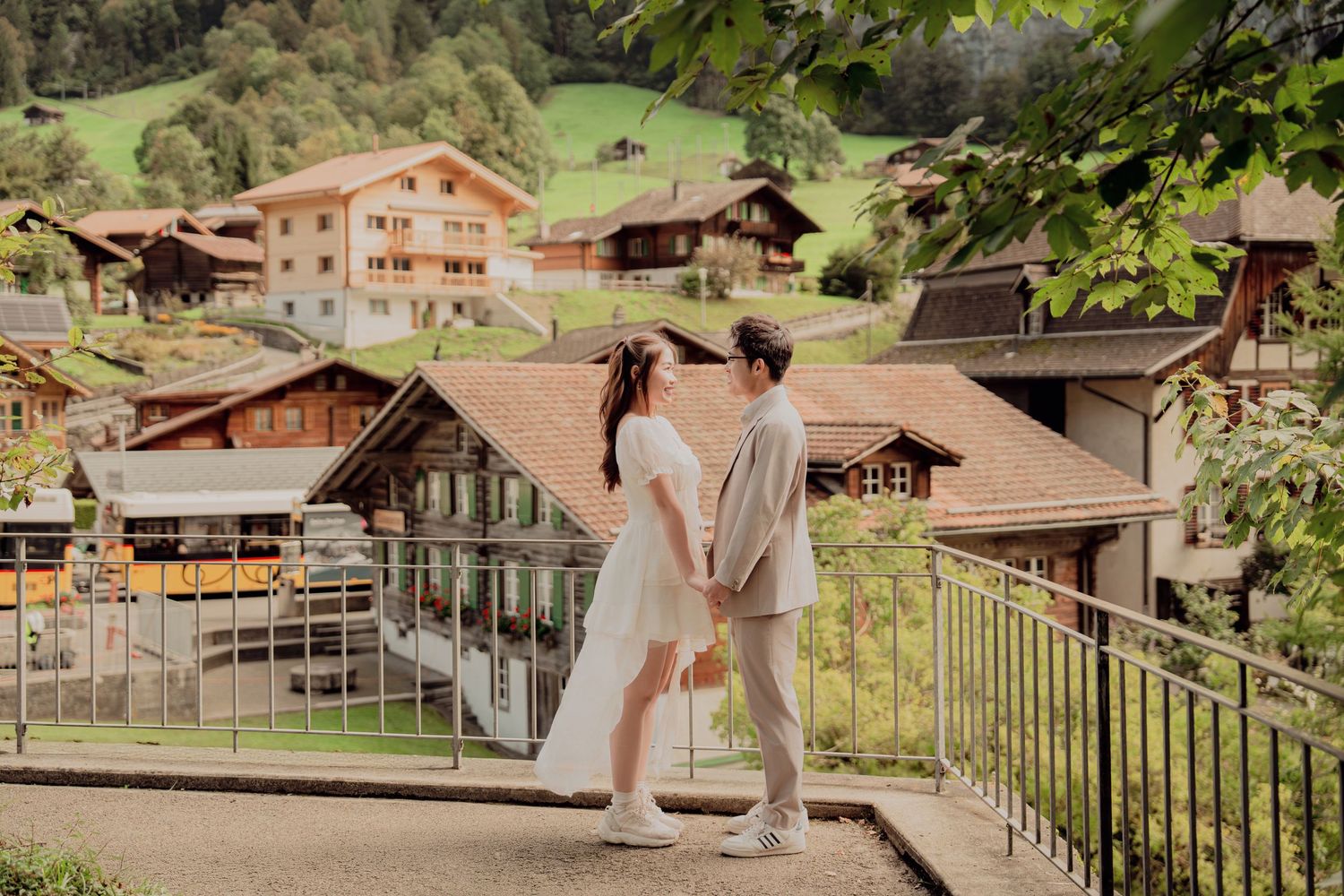 Couple holding hands on a balcony overlooking a picturesque Swiss alpine village.