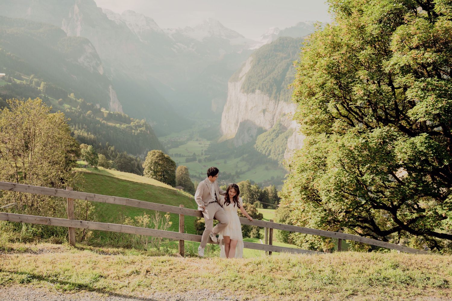 Wedding couple embracing on a sunlit hillside with majestic Swiss mountain valley in the background.
