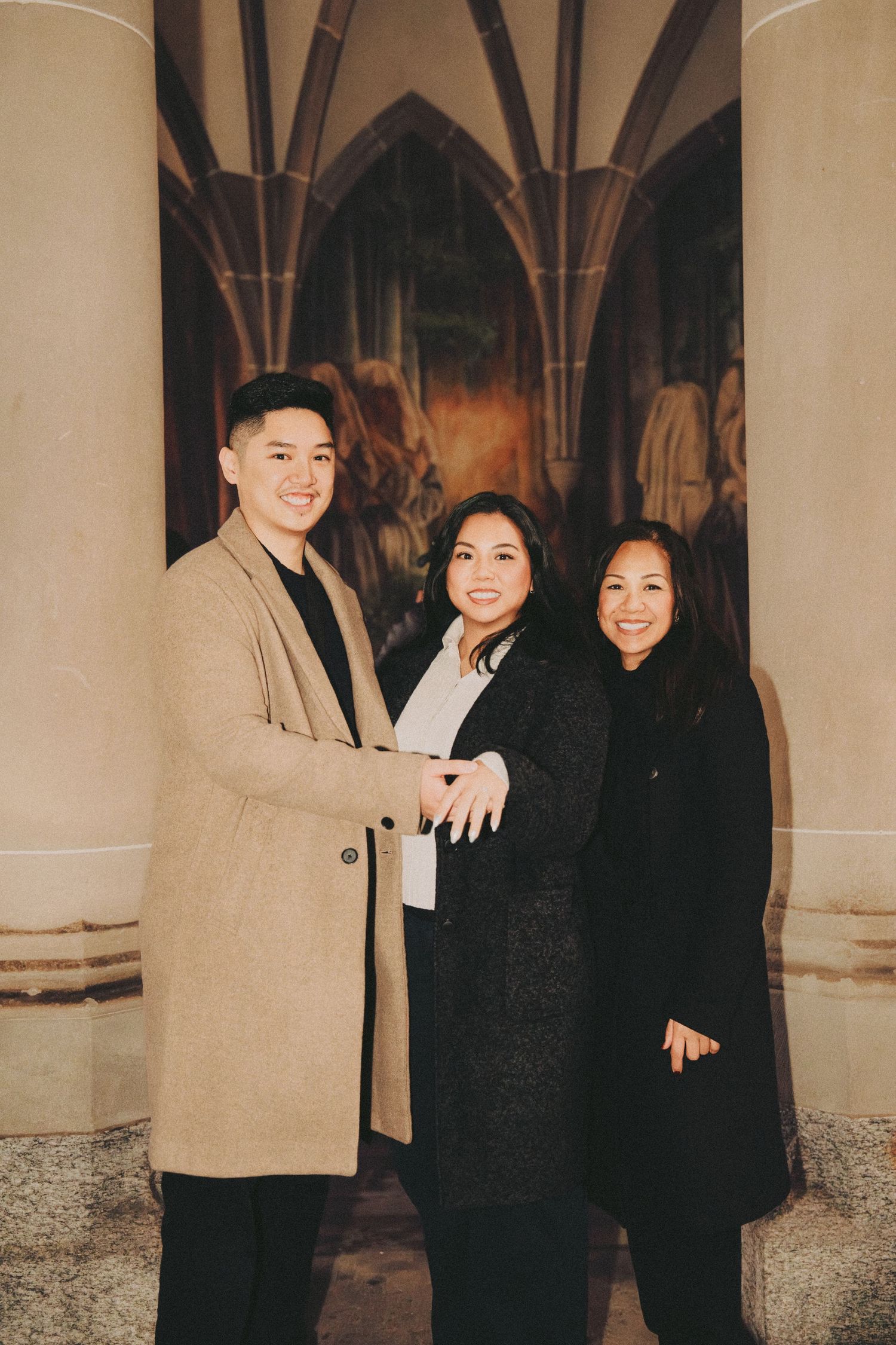 Three people posing together in front of a large religious mural inside a cathedral.