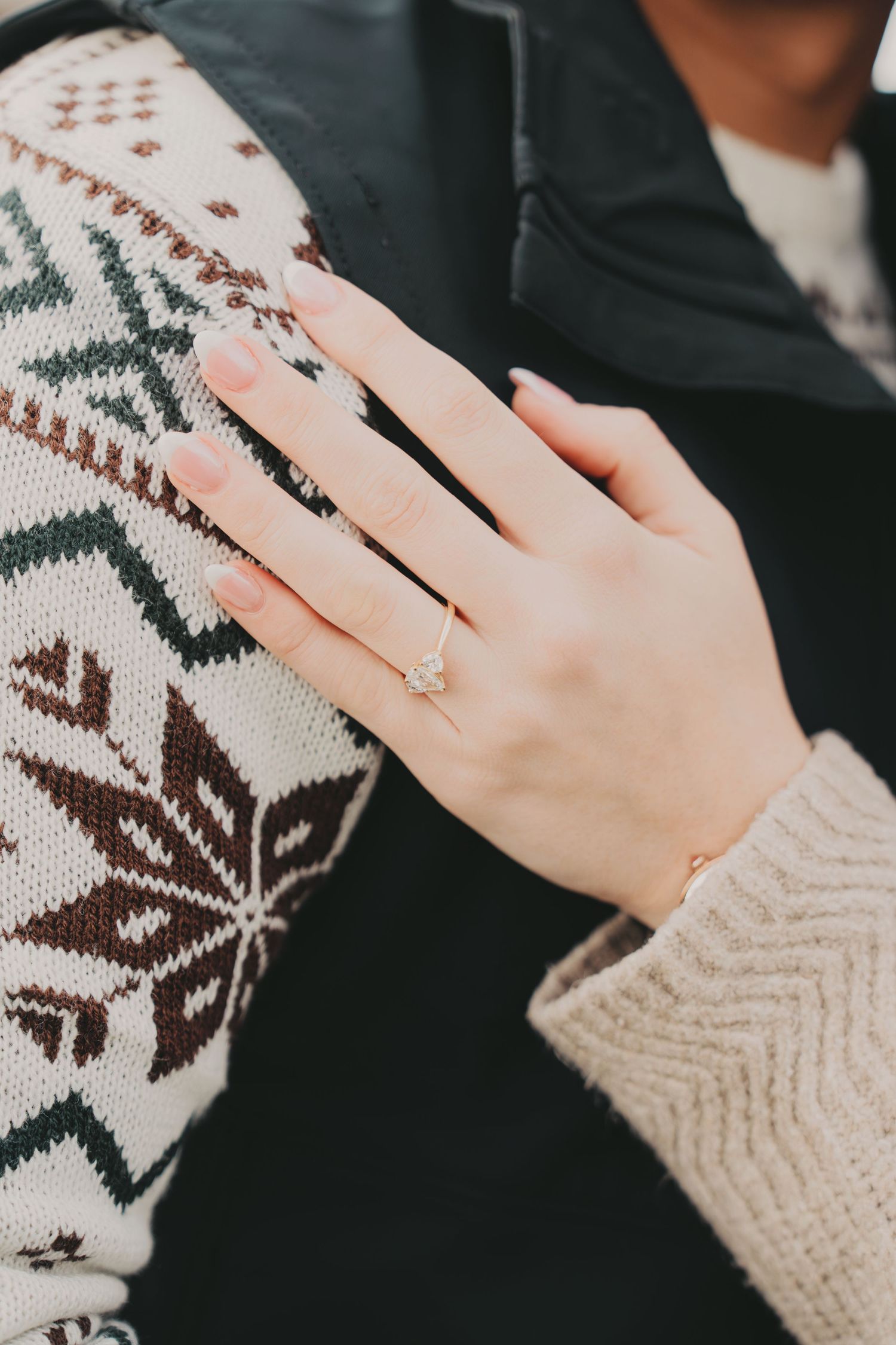 Close-up of womans hand showing elegant diamond engagement ring on mans sweater.