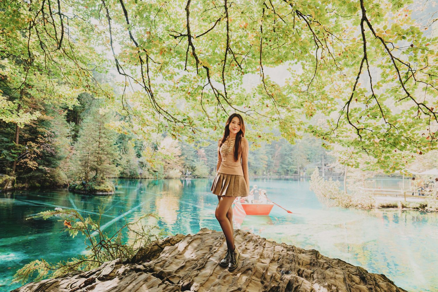 Young woman in beige outfit posing under tree branches by stunning turquoise alpine lake in autumn.