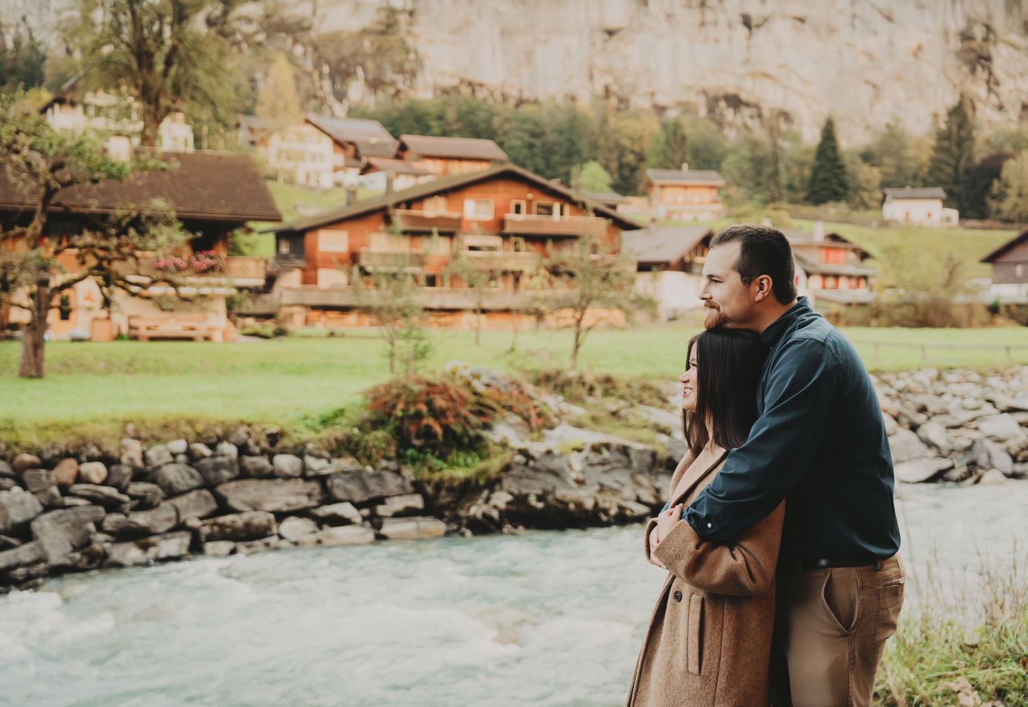 Couple standing together gazing at a scenic Swiss alpine river and mountain village.