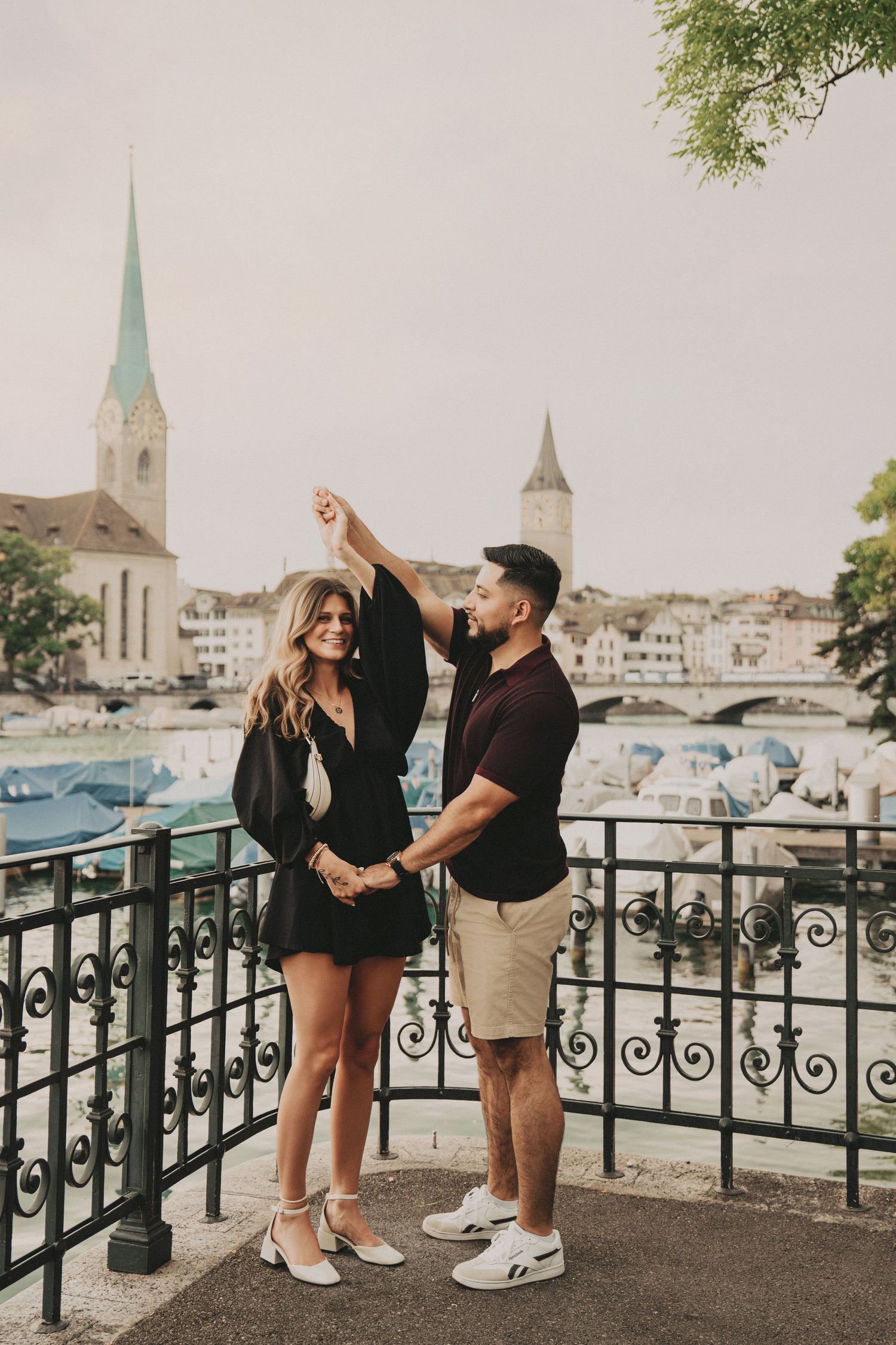 Smiling couple dancing on a scenic Zurich balcony with historic church towers and river views.