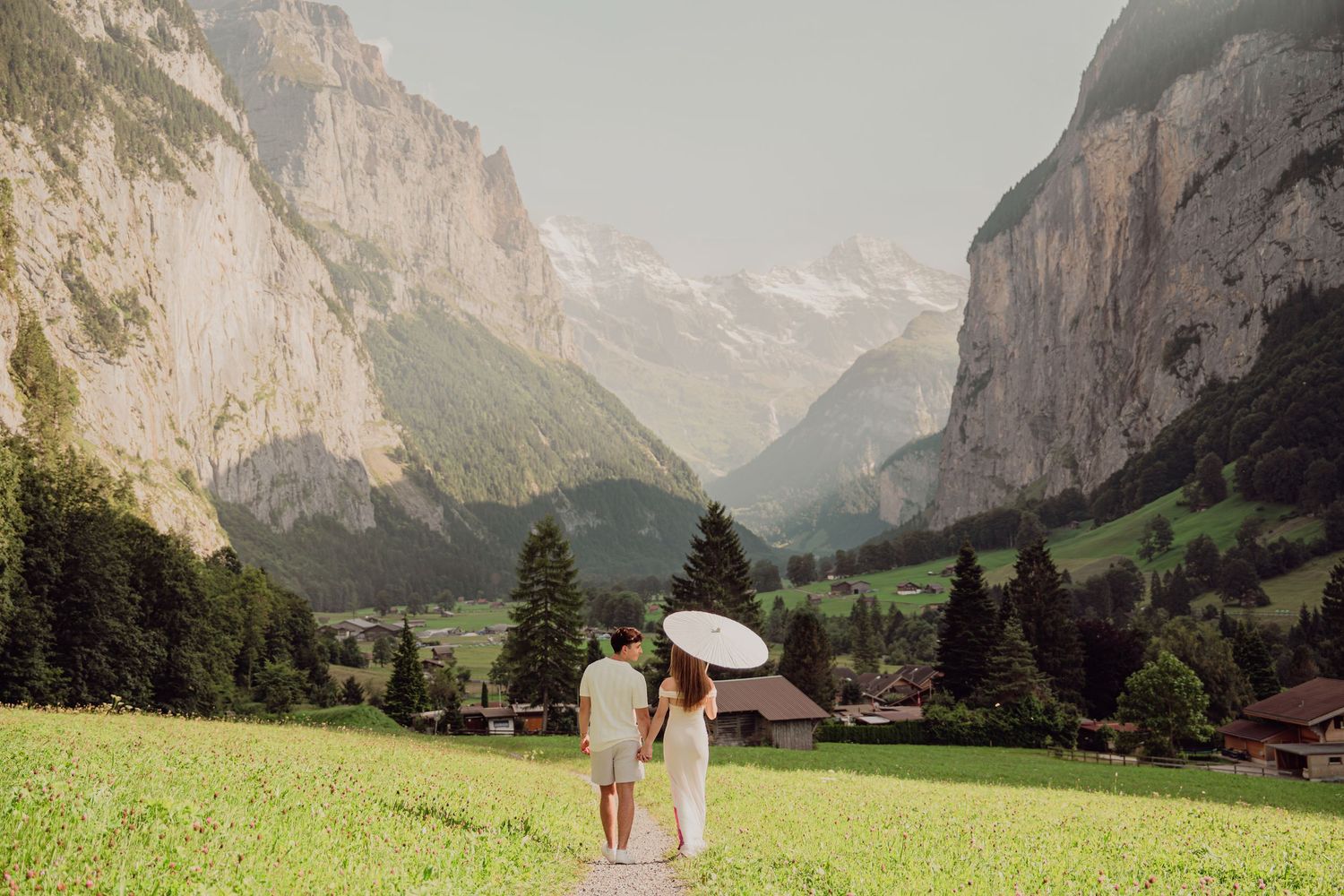 Couple walking hand in hand with a white parasol toward the stunning Lauterbrunnen valley.