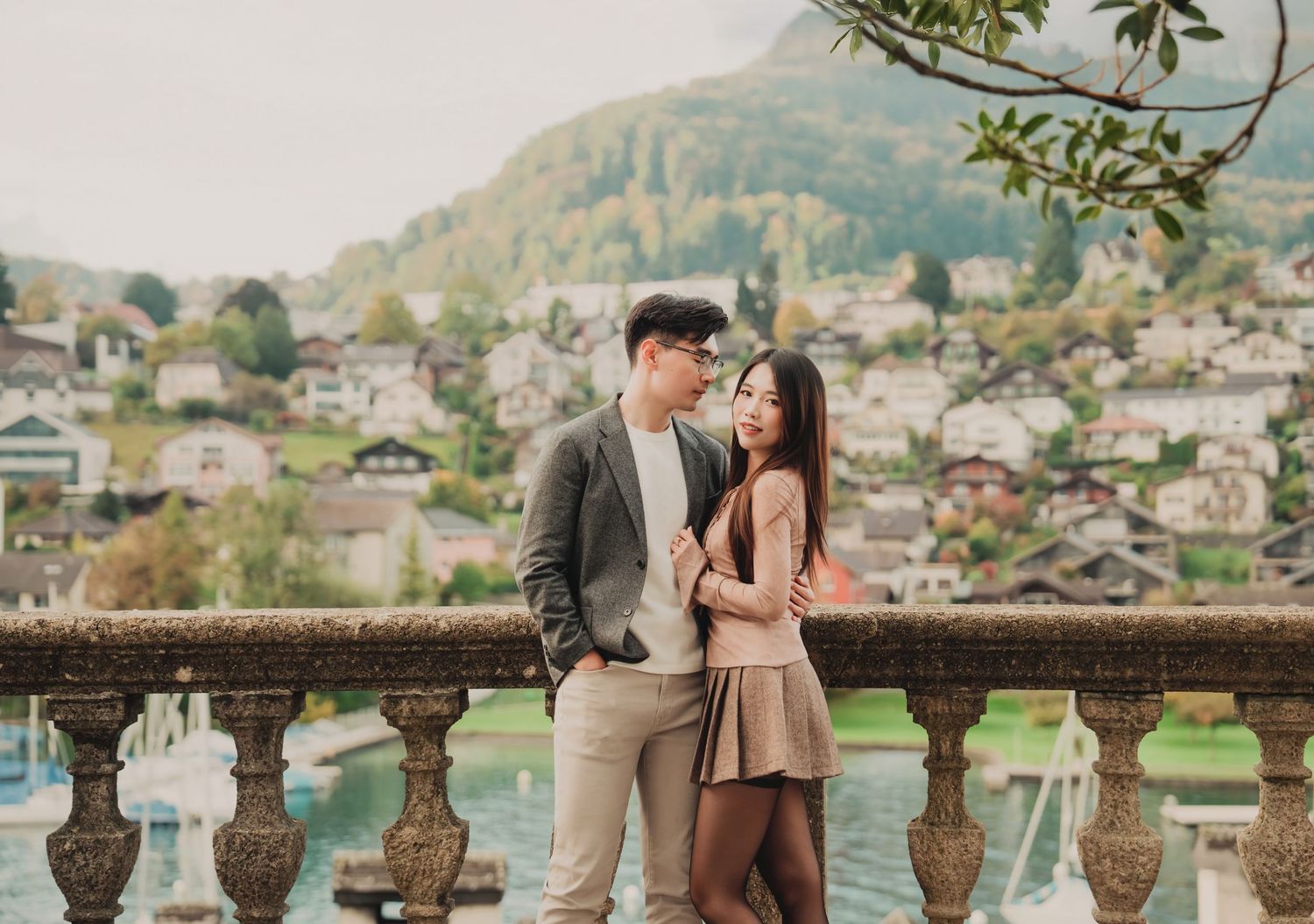 Couple sharing tender moment on ornate terrace overlooking picturesque lakeside Alpine village.
