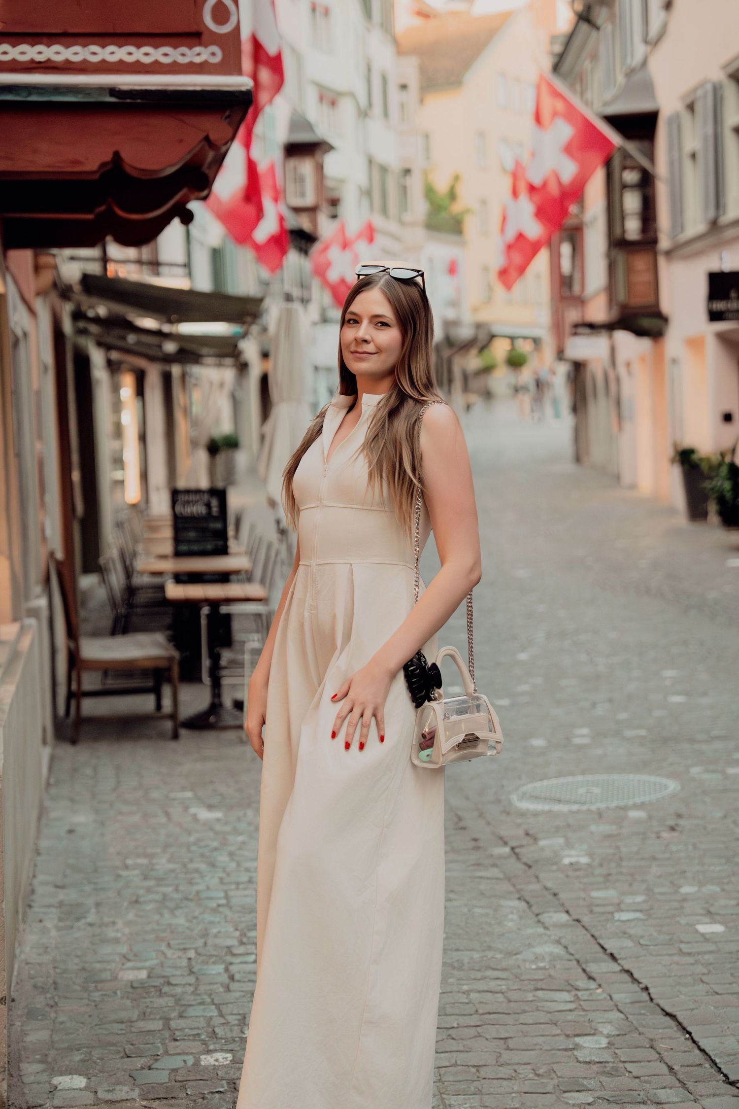 Stylish woman in beige dress walks cobblestone street decorated with Swiss flags in Zurich.