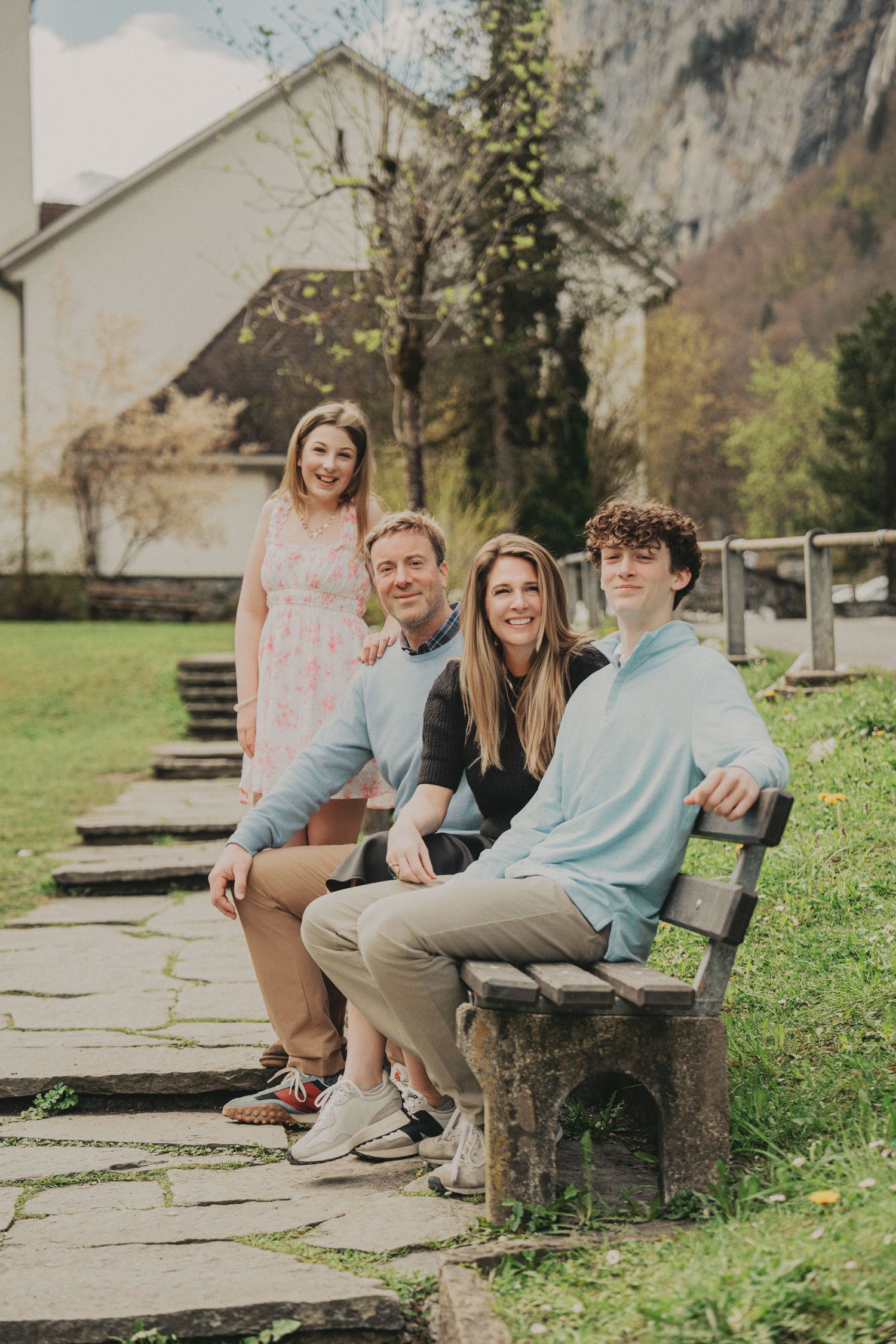 Family of four posing on a stone bench in a lush green Swiss village park.