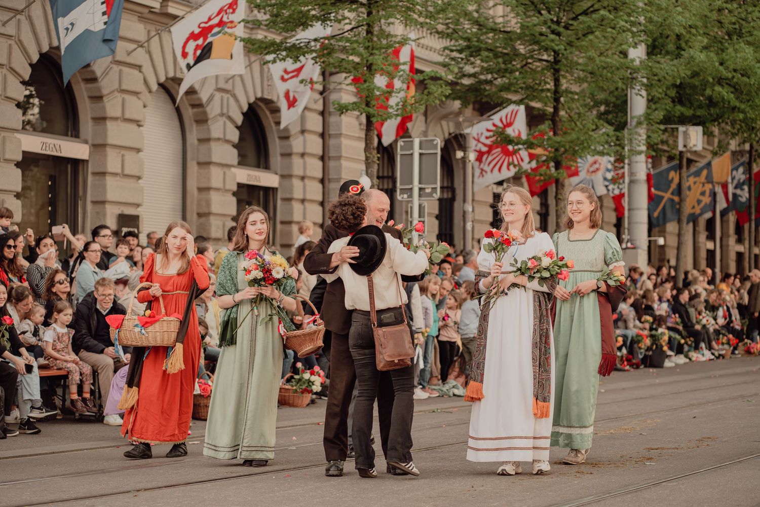 Women in traditional green and white folk dresses carrying flower baskets in a cultural street parade.