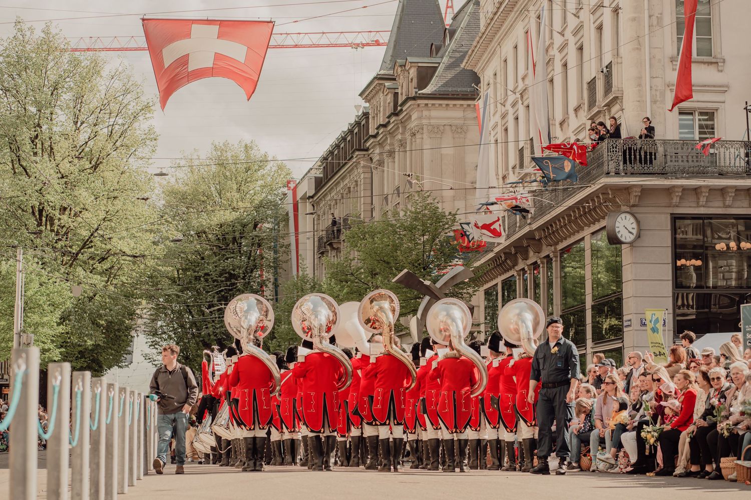 Drummers in matching red uniforms perform in formation during a street parade under Swiss flags.