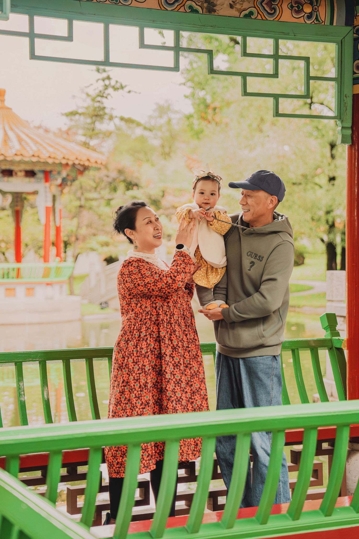 Grandparents lifting a joyful baby girl in a traditional Chinese garden pavilion.