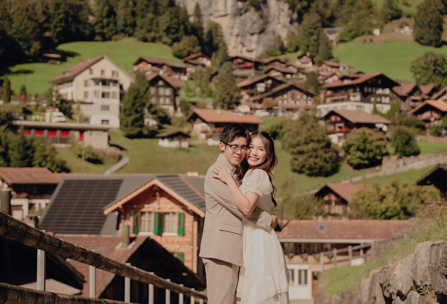 Couple embracing on a bridge with Swiss alpine village and green hillside in Lauterbrunnen, Switzerland.