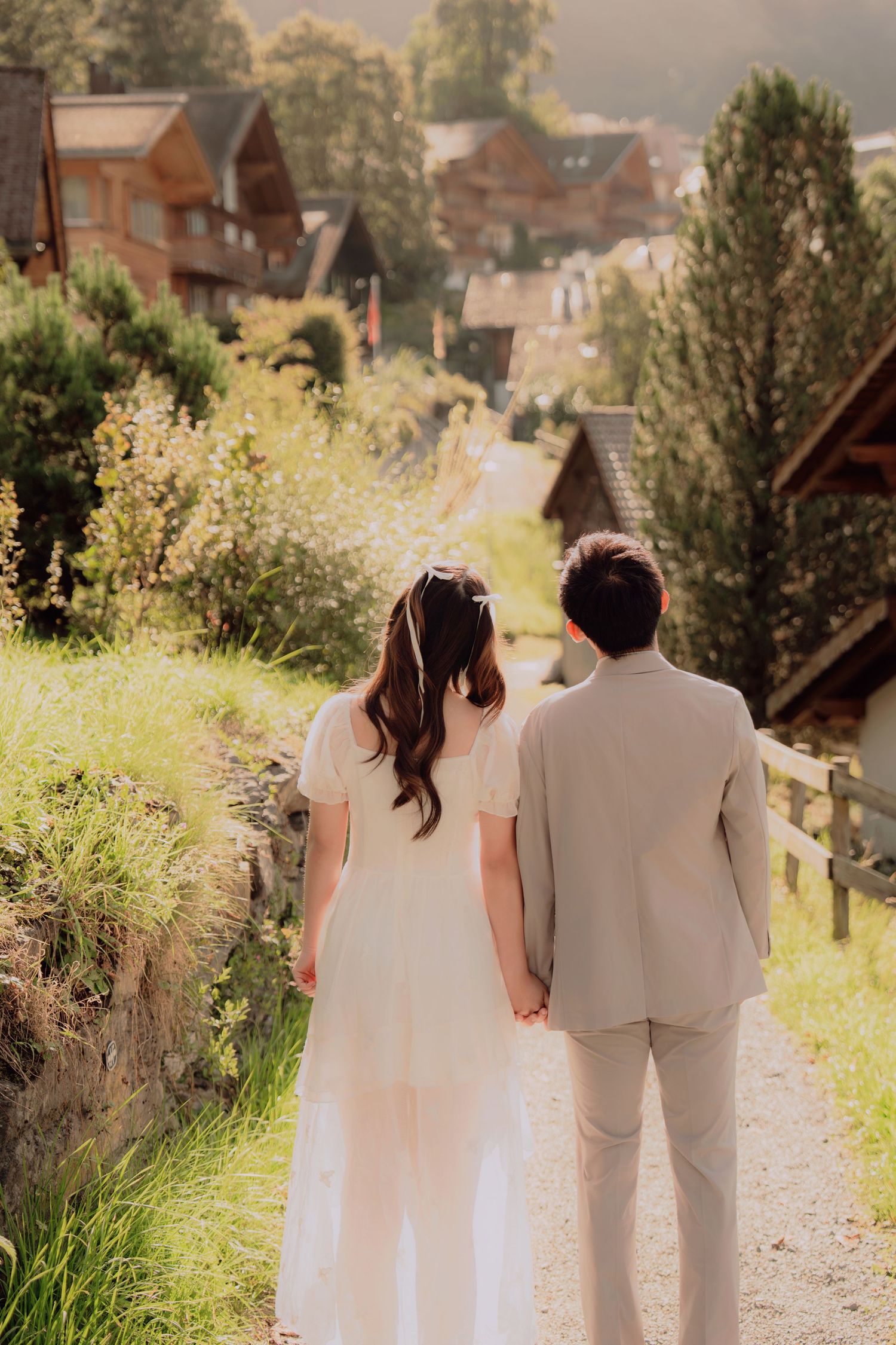 Wedding couple walking hand in hand along a peaceful path through a picturesque Swiss mountain village.